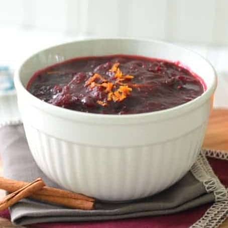square image of cranberry sauce with orange and cinnamon in a white serving bowl with orange zest on top