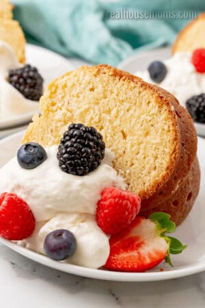 slice of cream cheese pound cake on a plate with whipped cream and fresh berries