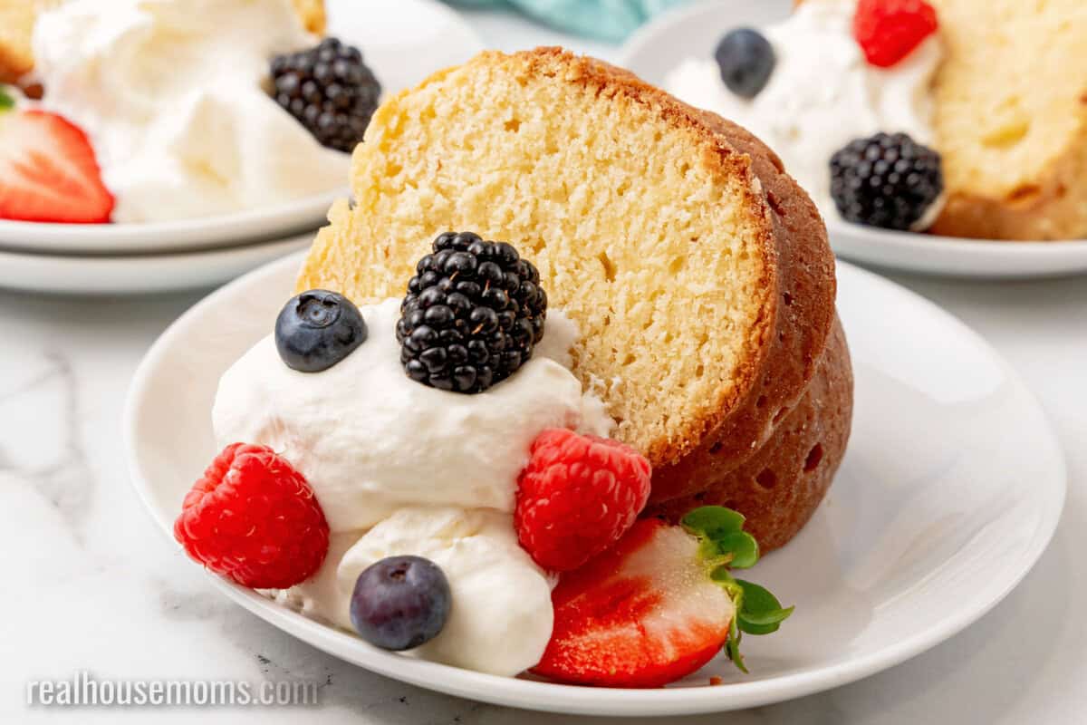 slice of cream cheese pound cake with whipped cream and fresh berries on a plate