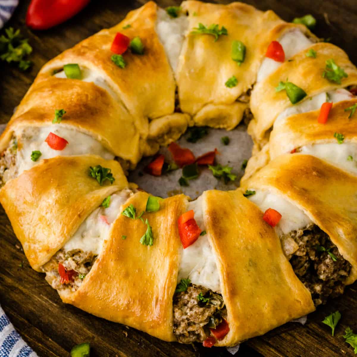 square image of a cream cheese & sausage crescent roll ring with dice red bell pepper and parsley on top