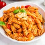 square image of a bowl of creamy caprese pasta with fresh basil for garnish