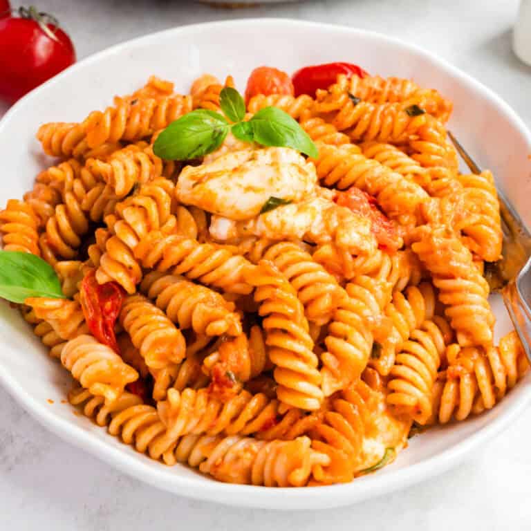 square image of a bowl of creamy caprese pasta with fresh basil for garnish