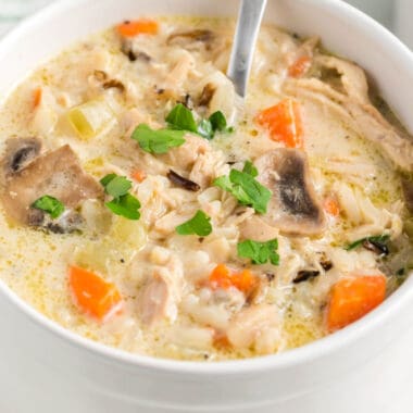 square image of creamy chicken adn wild rice soup in a bowl with a spoon