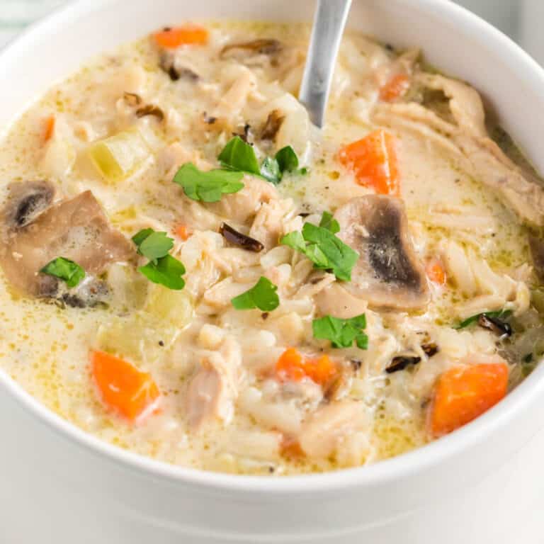 square image of creamy chicken adn wild rice soup in a bowl with a spoon