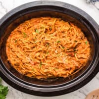 square image of creamy crock pot spaghetti in a slow cooker topped with parmesan and parsley