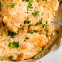 creamy garlic butter chicken in a skillet with one breast being lifted up from the pan with recipe name at bottom