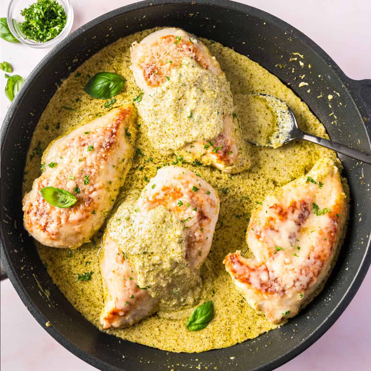 square image of creamy skillet pesto chicken in the skillet with a spoon