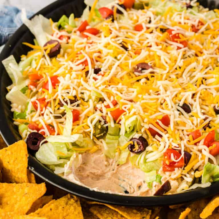 sqiare image of creamy taco dip with a bite taken out to show the layers