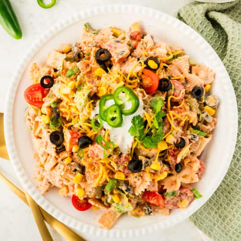 square image of creamy taco pasta salad topped with sour cream, cilantro, and jalapeno slices