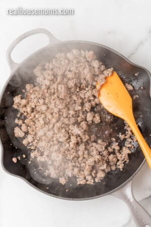 cooked and crumbled breakfast sausage in a skillet with rubber spatula