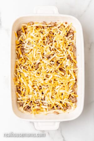 cooked breakfast sauce and shredded cheese spread over crescent roll dough in a baking dish