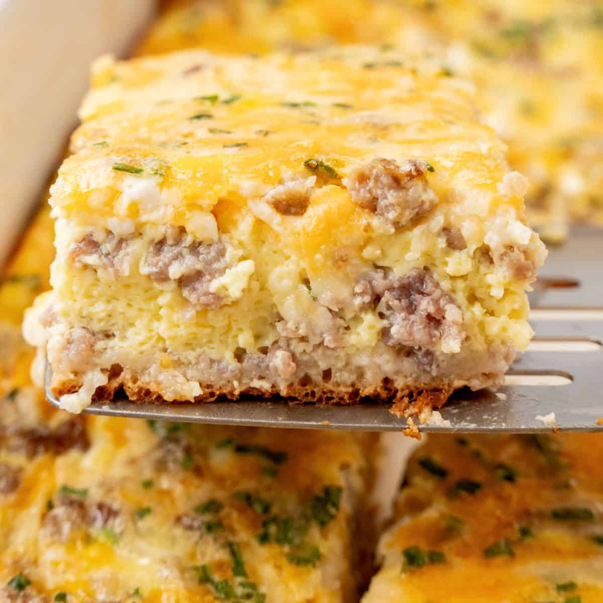 square image of a slice of crescent roll breakfast casserole on a metal spatula over the baking dish