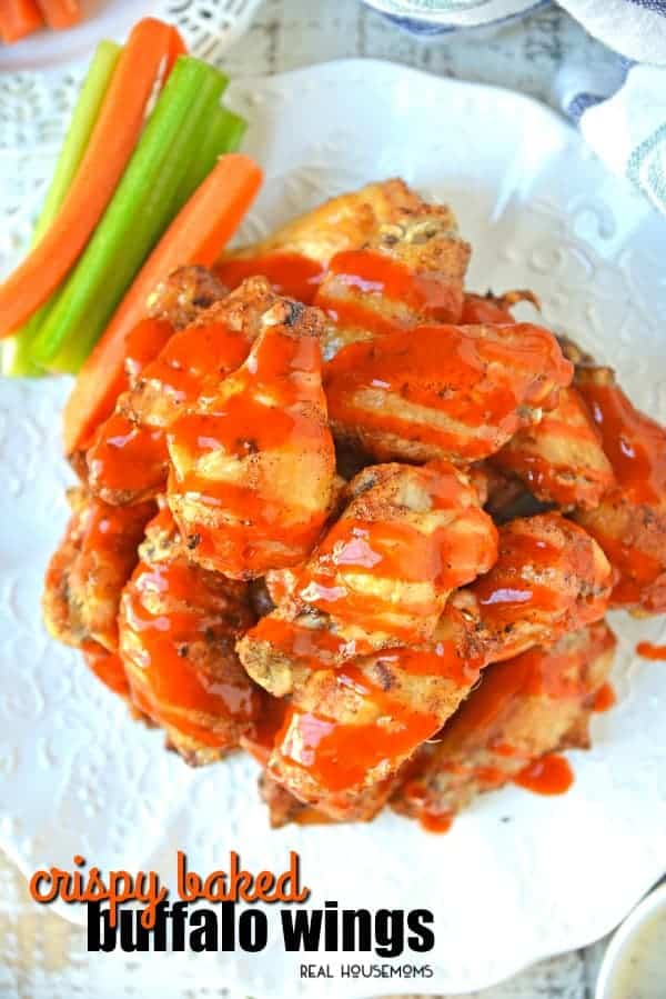Crispy Baked Buffalo Wings stacked on a plate, drizzled in buffalo sauce and served with celery and carrots
