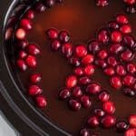 square image of cranberry apple cider with cranberries in crock pot