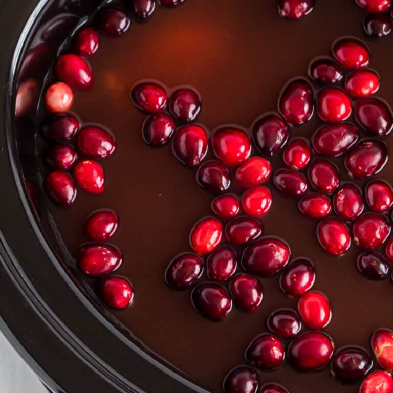square image of cranberry apple cider with cranberries in crock pot