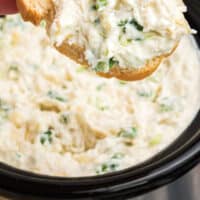 crock pot artichoke crab dip on a slice of bread over the slow cooker with recipe name at the bottom