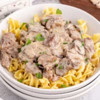 square image of crock pot beef stroganoff served over egg noodles in a bowl