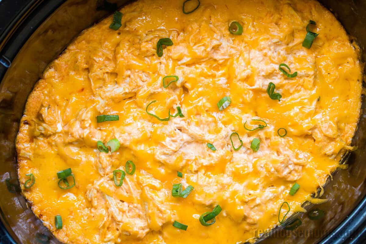 cooked buffalo chicken dip topped with sliced green onions in a crockpot