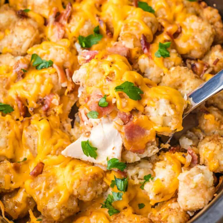 square image of a spoonful of crock pot cheesy chicken, bacon & tater tot bake over the slow cooker