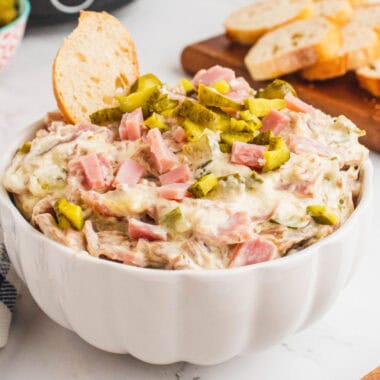 square image of crock pot cheesy cuban dip in a serving bowl with a bread slice stuck into the dip