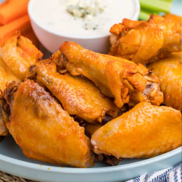 square image of crock pot chicken wings piled up on a plate next to a bowl of blue cheese dressing
