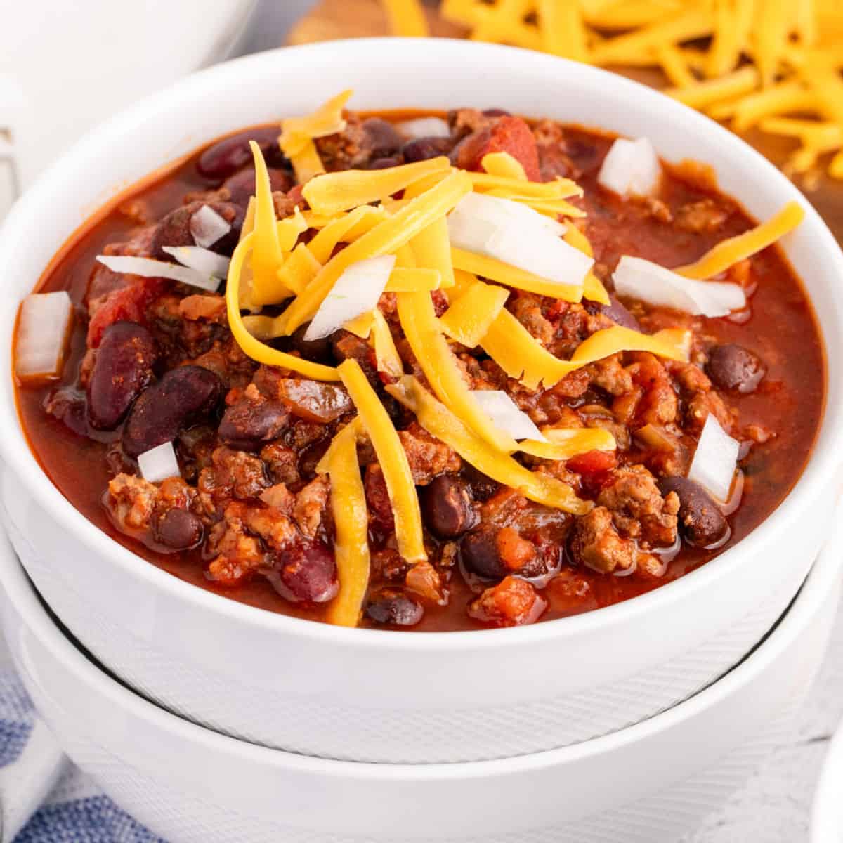 square image of crock pot chili topped with cheddar cheese and white onion