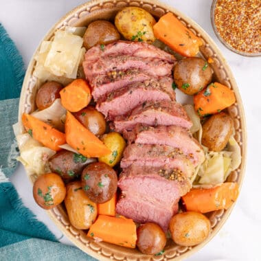 square image of crock pot corned beef and cabbage sliced and arrange on a platter with potatoes and carrots
