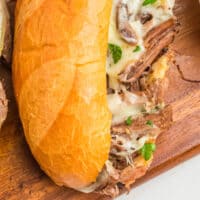 close up of a crock pot french dip sandwich on a cutting board with recipe name at the bottom