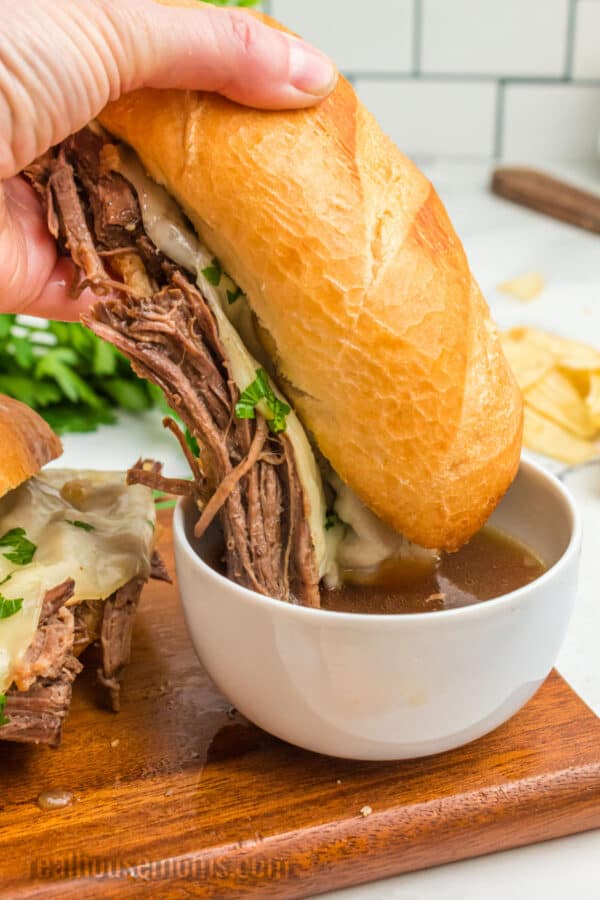 crock pot french dip sandwich being dipped into a bowl of au jus