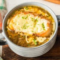 square image of a bowl of crock pot french onion soup topped with chopped parsley