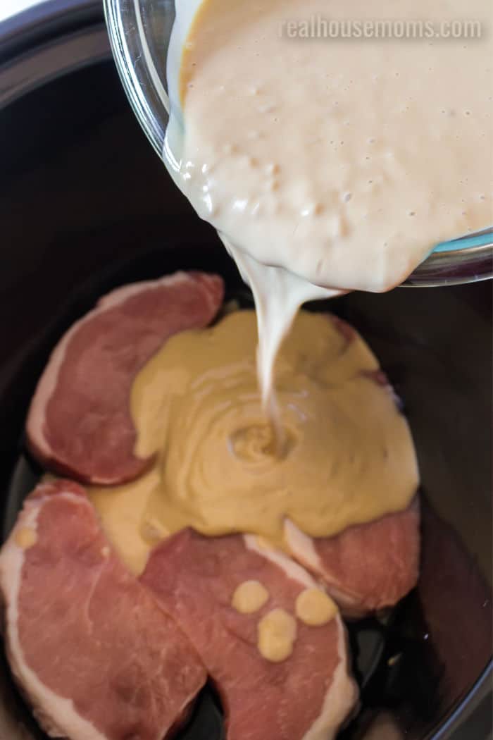 sauce being poured over pork chops in a crock pot