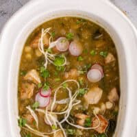 crock pot pozole in a slow cooker with sliced radishes and shredded green cabbage with the title of the post on top of the image in pink and black lettering