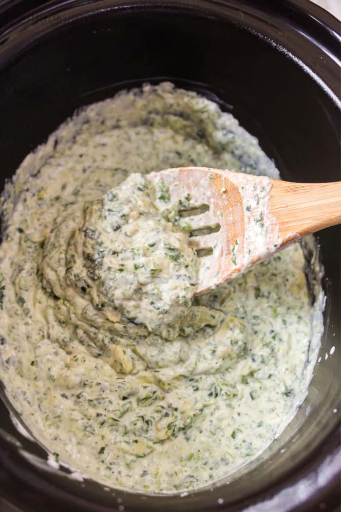 crock pot spinach artichoke dip after cooking with a portion on a serving spoon