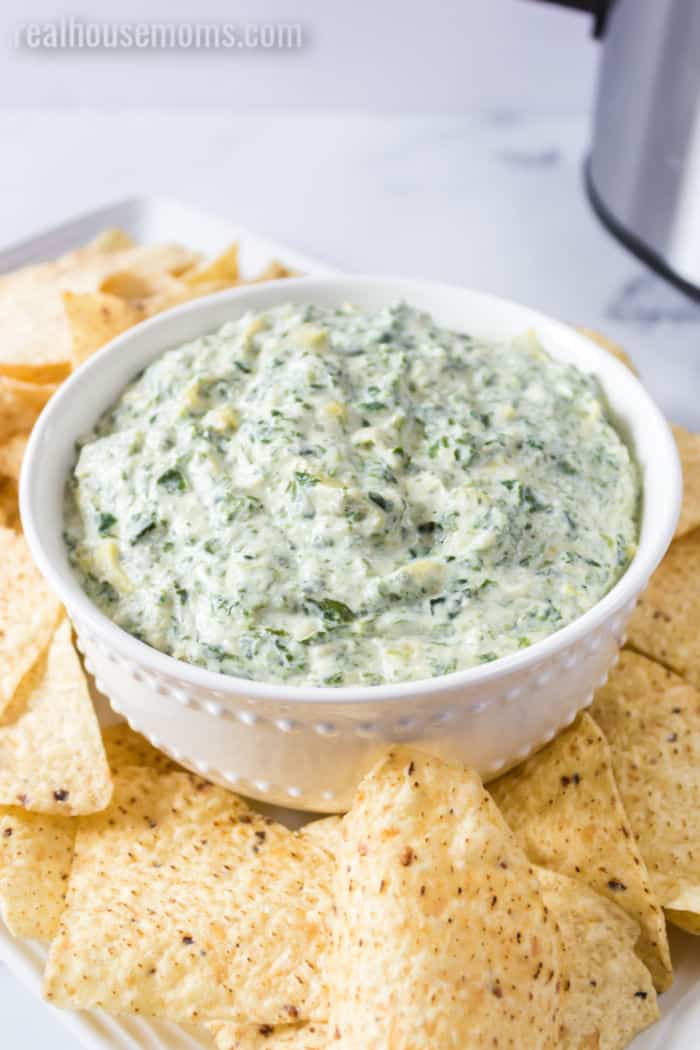 crock pot spinach artichoke dip in a bowl surrounded by tortilla chips