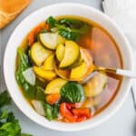square image of crock pot vegetable soup with a spoon in the bowl