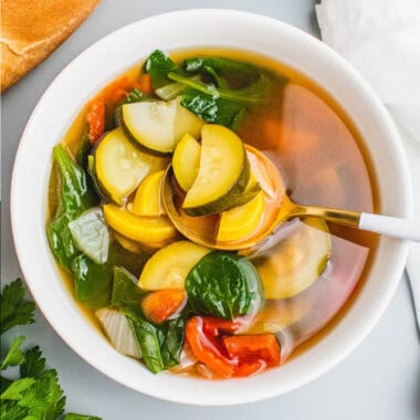 square image of crock pot vegetable soup with a spoon in the bowl