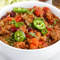 square image of crock pot weight watchers chili in a bowl with sliced jalapeno and green onions on top