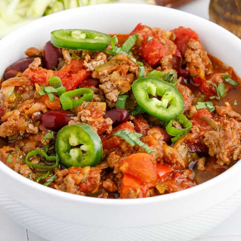 square image of crock pot weight watchers chili in a bowl with sliced jalapeno and green onions on top