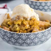 square image of apple cobbler in a bowl topped with ice cream