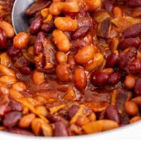 spoon of baked beans being taken from a crock pot with recipe name at the bottom