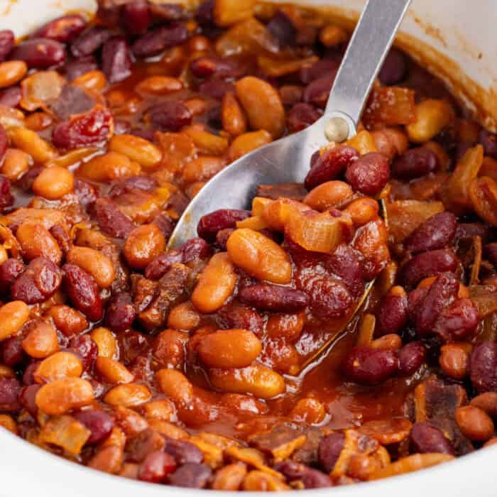 square image of a serving spoon of crockpot baked beans being taken from the slow cooker