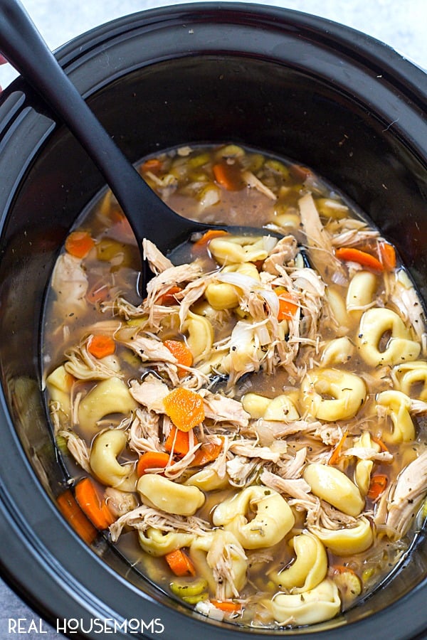 Crock Pot Chicken Tortellini Soup just after cooking with a ladle ready to portion the soup into bowls