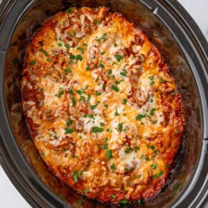 square image of crockpot lasagna topped with chopped parsley in a slow cooker