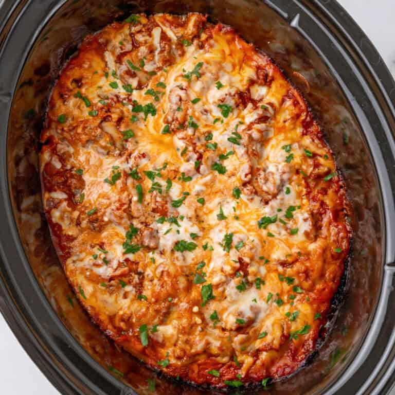 square image of crockpot lasagna topped with chopped parsley in a slow cooker