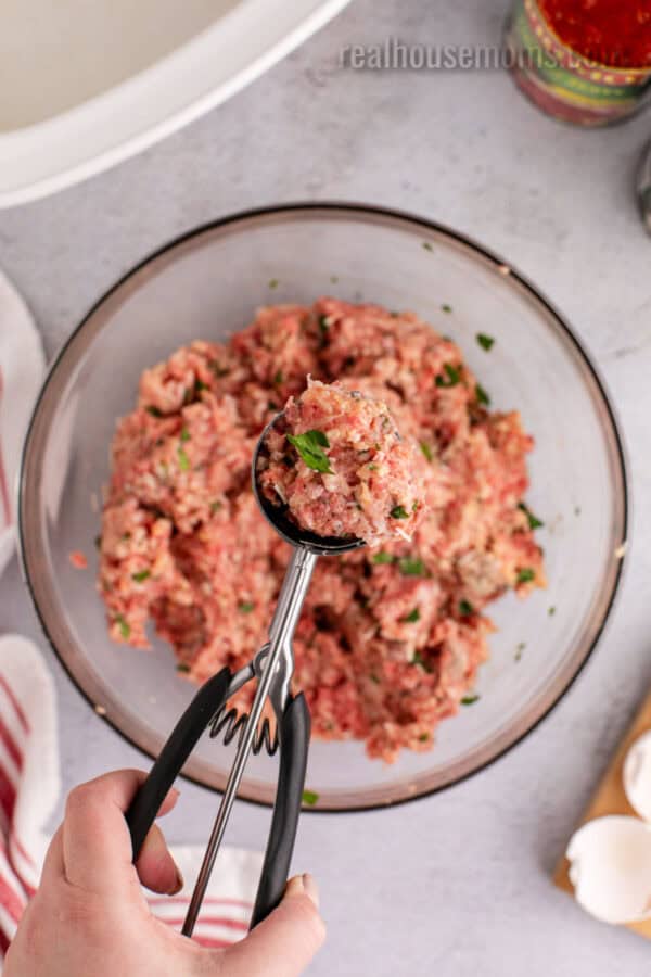 large cookie scoop of meatball mixture over the bowl