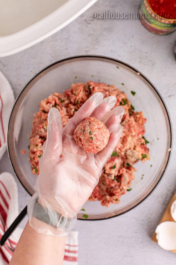 meatball mixture scoop rolled into a ball sitting on a gloved hand over the bowl