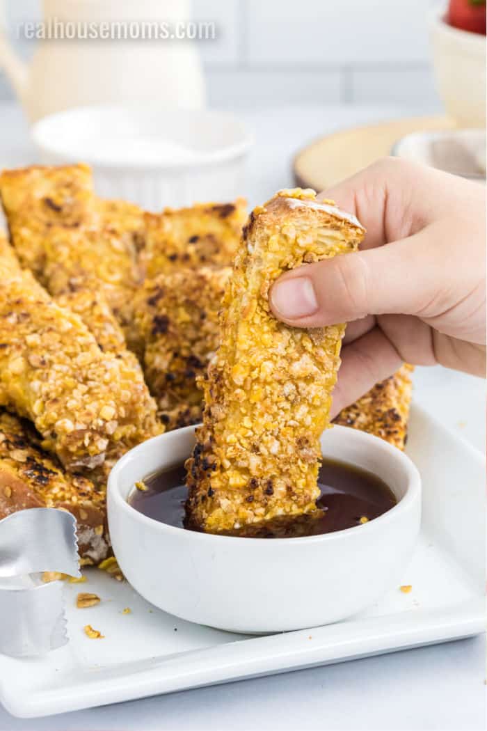 french toast stick being dipped into a bowl of syrup