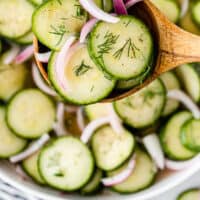 cucumber and onion salad on a wooden spoon over the serving bowl with recipe name at the bottom