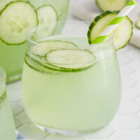 square image of cucumber punch with a green striped straw and cucumber slice for garnish