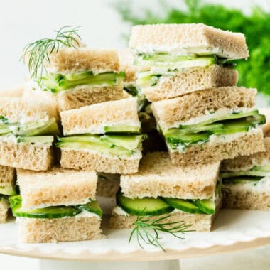 square image of cucumber sandwich squares arranged on a cake stand